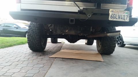 1992 Ford Bronco - The rear underside of a vehicle is shown, with a focus on the axle and exhaust pipe, parked on a paved driveway.