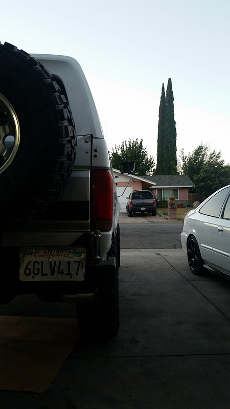 1992 Ford Bronco - A silver 1992 Ford Bronco is parked in a driveway, seen from the rear with a spare tire mounted.