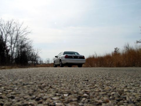 2000 Ford Crown Victoria - Rear view of a 2000 Ford Crown Victoria on a rural road under an overcast sky.