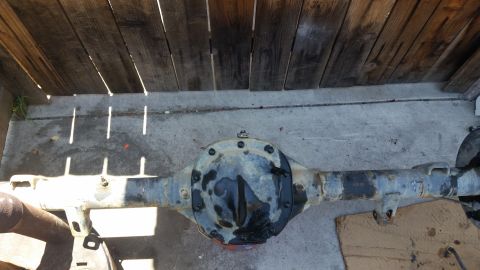 1992 Ford Bronco - Rear axle assembly shown from above, resting on a concrete surface under a wooden fence. The differential cover is visible.
