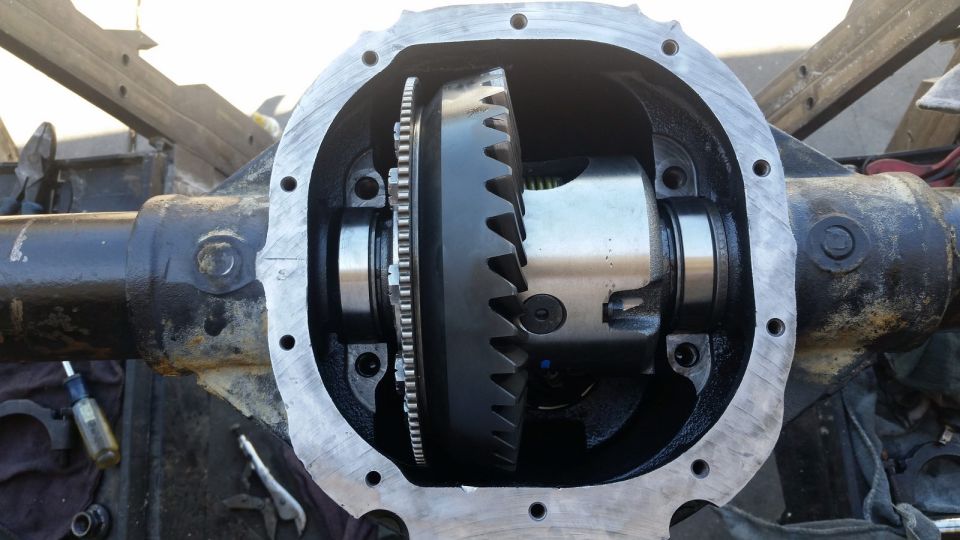 Open differential housing with gears and bearings visible. Tools and rags are on the ground nearby