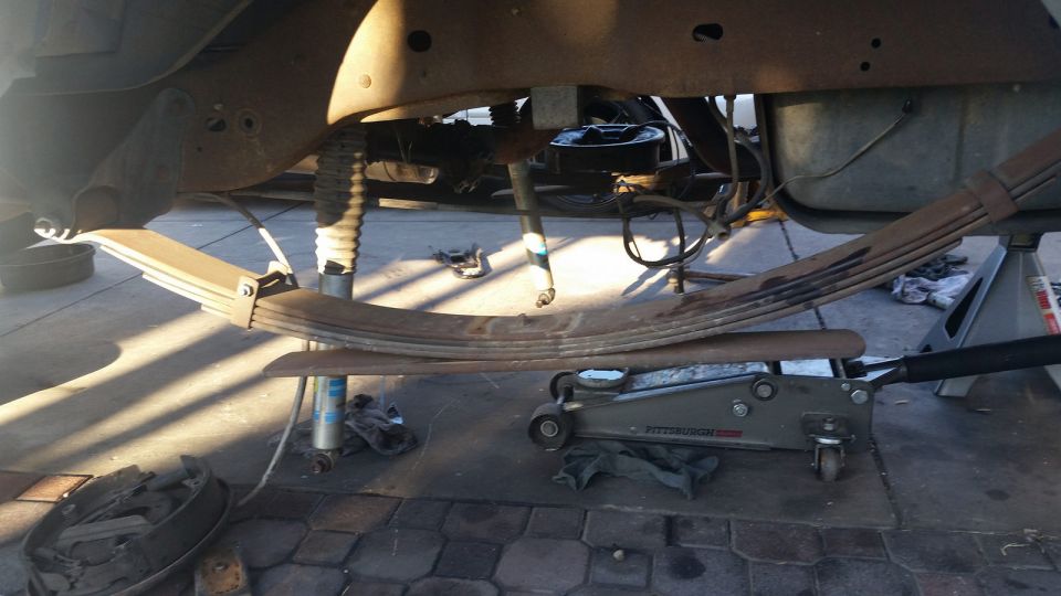 Leaf spring assembly supported by a jack and jack stands, with a drum brake visible