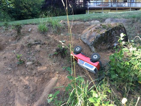 1989 Ford Bronco - Toy truck has tipped over on a dirt slope next to a large rock.