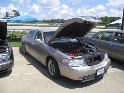 2004 Ford Crown Victoria - Two cars are parked side-by-side with hoods open at an outdoor event. A third car is visible on the right.