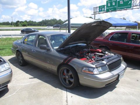 2004 Ford Crown Victoria - This Ford Crown Victoria has its hood open, revealing the engine bay and red accents on the fender. Another Crown Victoria is parked behind…