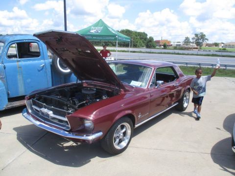 2004 Ford Crown Victoria - A maroon 1967 Ford Mustang coupe is displayed with its hood open, parked beside a blue truck.