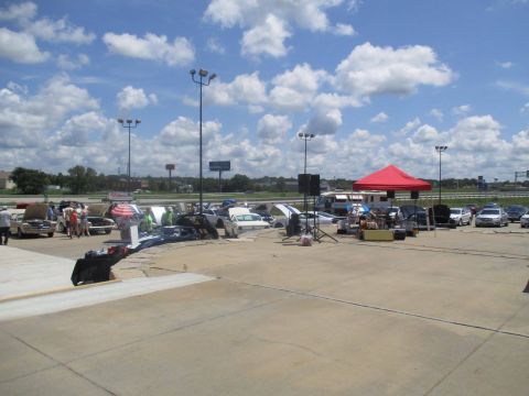 2004 Ford Crown Victoria - Outdoor car show event with multiple vehicles and vendor tents under a partly cloudy sky.
