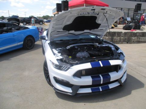 2004 Ford Crown Victoria - A white Ford Mustang with racing stripes is displayed with its hood open, next to a blue convertible Mustang.