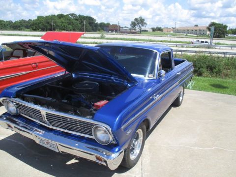 2004 Ford Crown Victoria - A blue 1960 Ford Falcon Ranchero is parked outside with its hood up, next to another vehicle.