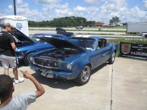 2004 Ford Crown Victoria - A blue 1965 Ford Mustang fastback, modified with white racing stripes and an open hood, is displayed at an outdoor event.