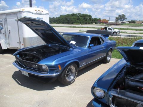 2004 Ford Crown Victoria - Two blue Ford Mustangs, one a 1970 Mach 1, are parked with hoods open.