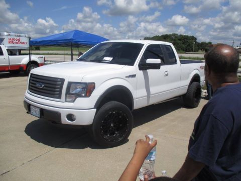 2004 Ford Crown Victoria - A white Ford F-150 pickup truck is parked outside under a blue tent with other vehicles present.