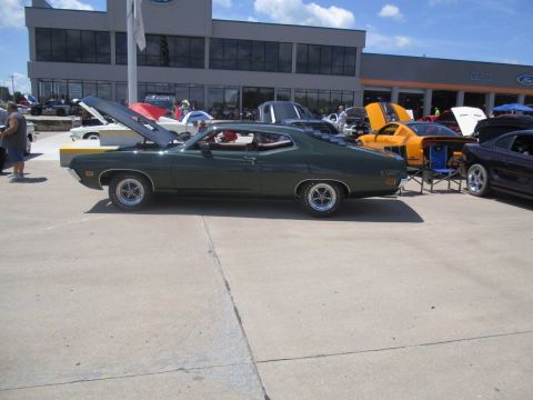 2004 Ford Crown Victoria - A dark green 1970 Ford Torino coupe is parked on a lot in front of a Ford dealership.
