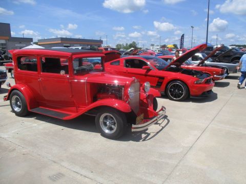 2004 Ford Crown Victoria - A classic red sedan is displayed alongside newer Ford Mustangs under a partly cloudy sky.