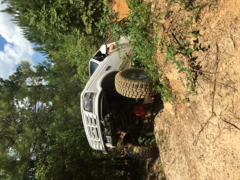 1989 Ford Bronco - Pickup truck with large tires is stuck on a dirt embankment during off-roading.