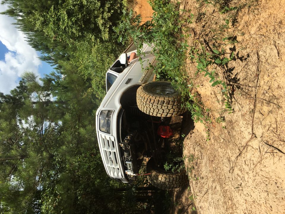 White pickup truck with large tires stuck on a dirt embankment
