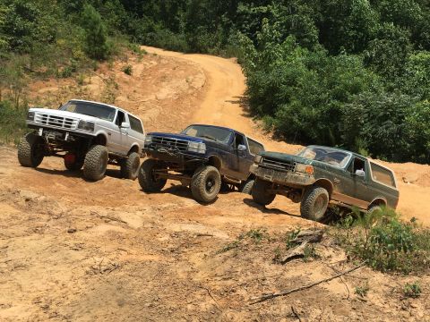 1989 Ford Bronco - Three Ford Broncos navigate a challenging off-road trail, their lifted suspensions and capabilities.