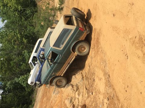 1989 Ford Bronco - Multiple SUVs navigate a rocky, dirt path surrounded by trees.