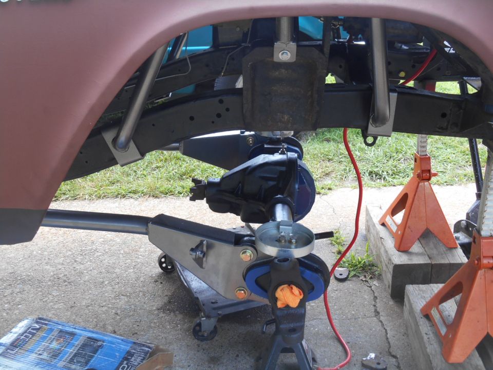 Close-up of a vehicle's rear axle assembly being worked on, supported by jacks and stands
