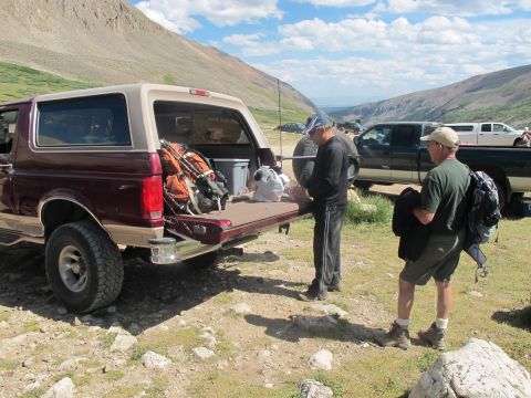1996 Ford Bronco - Two men prepare camping gear next to a 1996 Ford Bronco in a mountainous area.