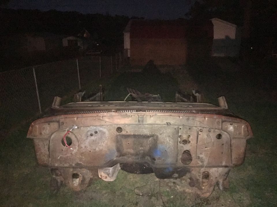 Rusted vehicle front end with exposed engine bay, wires visible, sitting on grass