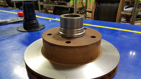 1973 Ford F-100 - A rusty brake rotor with a metal hub assembly is shown on a blue surface with a yellow measuring tape in the background.