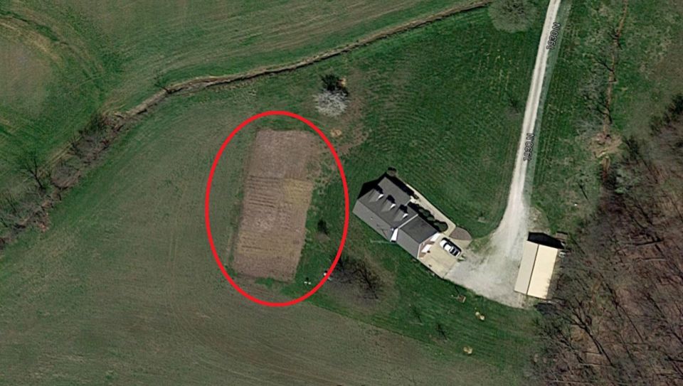 Aerial view of a house with a driveway and a red circle around a tilled garden plot