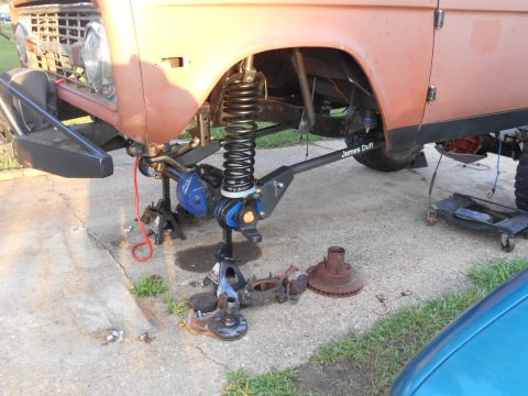 1972 Ford Bronco - The front suspension of a vintage Ford Bronco is disassembled and supported by jack stands. A large coil spring is visible, along with brak…