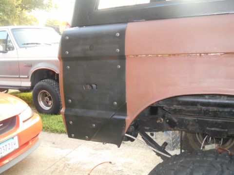 1972 Ford Bronco - A close-up side view of a classic Ford Bronco's rear quarter panel, showing a black metal plate bolted over the rusted brown body. Another…
