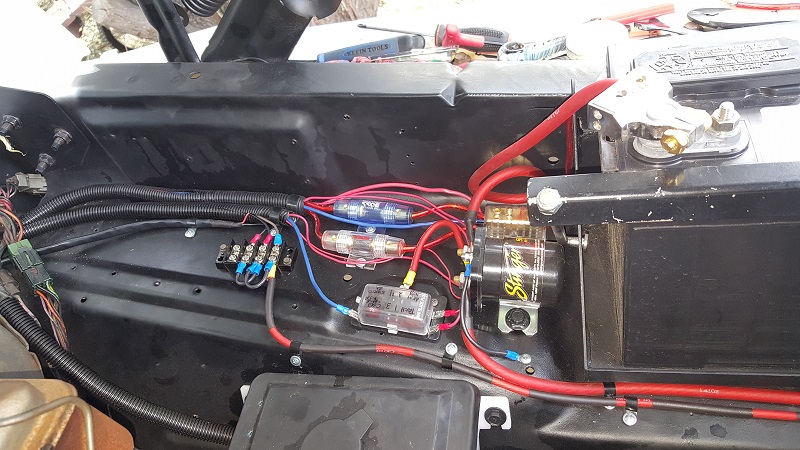 Vehicle engine bay wiring with battery, fuse boxes, and colorful wires.
