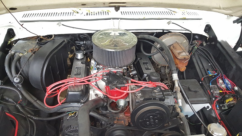 Classic Ford Bronco V8 engine bay with chrome air cleaner and red spark plug wires.