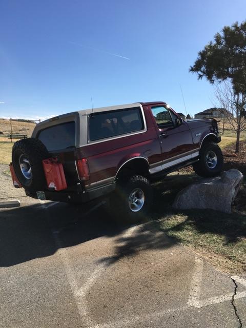 1996 Ford Bronco - A red Ford Bronco is parked on a rocky incline with its rear tire on a large boulder. A spare tire is mounted on the rear of the vehicle, a…