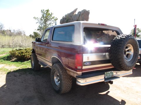 1996 Ford Bronco - The rear passenger side of a maroon 1996 Ford Bronco is shown parked on a dirt road with a spare tire mounted on the back. The vehicle has…