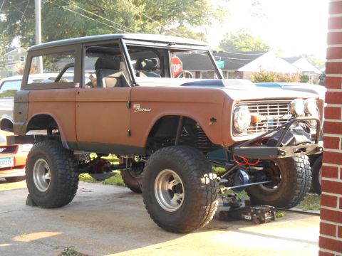 1972 Ford Bronco - A highly modified, lifted first-generation Ford Bronco with large off-road tires sits on a paved surface. The vehicle has a rusty brown ext…