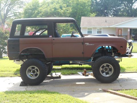1972 Ford Bronco - A lifted, brown 1972 Ford Bronco is parked on a concrete driveway in front of a house. The vehicle has a black hardtop and large off-road t…