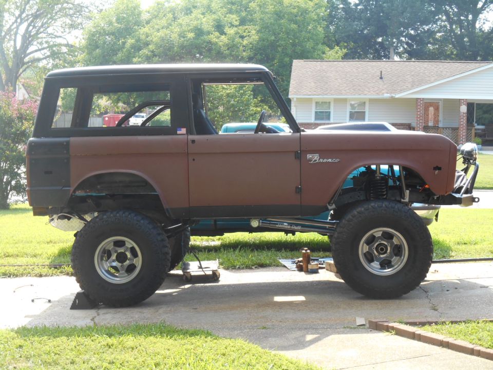 Lifted brown 1972 Ford Bronco with black hardtop and off-road tires parked on driveway.