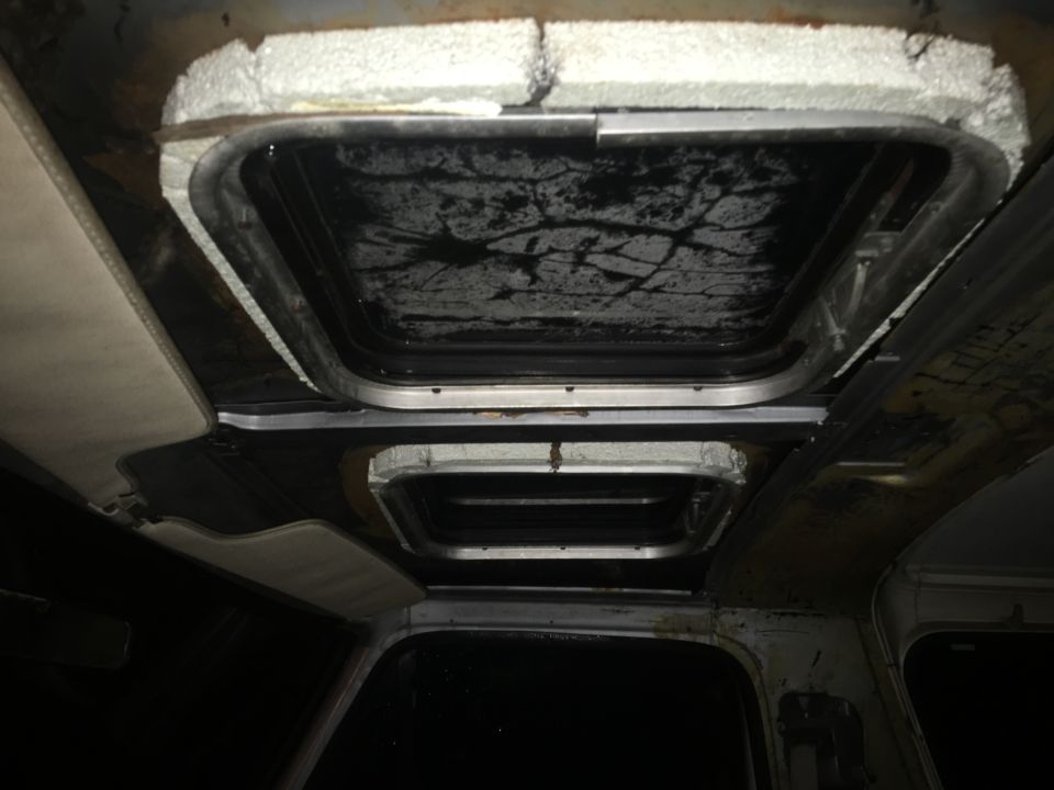 Interior view of a vehicle roof with two sunroofs, showing damaged seals and insulation.