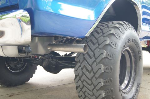 1979 Ford Bronco - Close-up view of the rear tire and exhaust pipe of a blue Ford Bronco. The large, aggressive tread of the off-road tire is prominent, with…