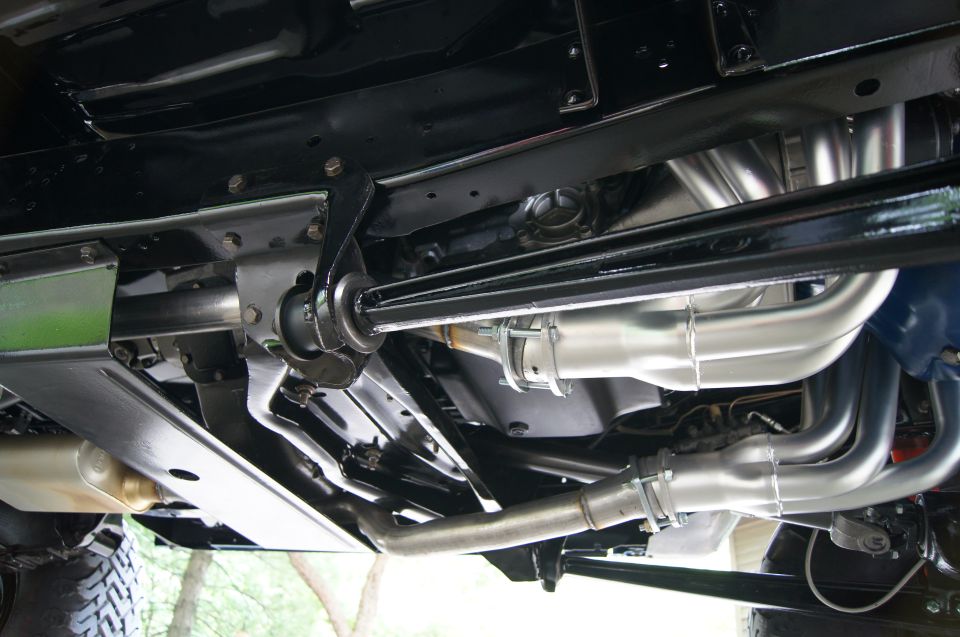 Underside of a classic SUV showing custom exhaust headers, pipes, and mufflers.