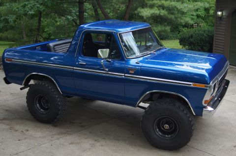 1979 Ford Bronco - A bright blue 1979 Ford Bronco is parked on a concrete driveway in front of a house with trees in the background. The Bronco has large off-…