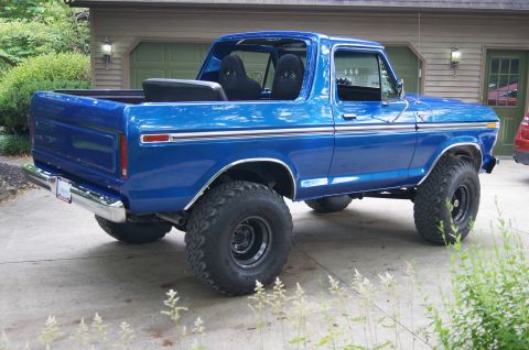 1979 Ford Bronco - The rear passenger side of a lifted, bright blue 1979 Ford Bronco is shown parked on a concrete driveway in front of a garage.