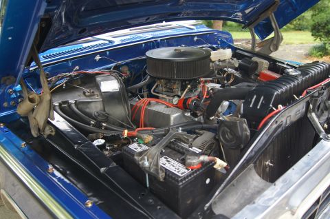 1979 Ford Bronco - The open hood of a blue classic Ford Bronco reveals a detailed view of its engine bay, showcasing the V8 engine, air filter, battery, and v…
