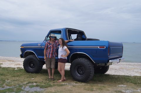 1979 Ford Bronco - A man and a young woman pose next to a lifted, bright blue Ford Bronco with large off-road tires. They are standing on a grassy area next t…