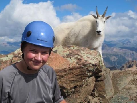 1996 Ford Bronco - A young person wearing a blue helmet smiles at the camera, with a mountain goat standing on a rock behind them. The background shows a moun…