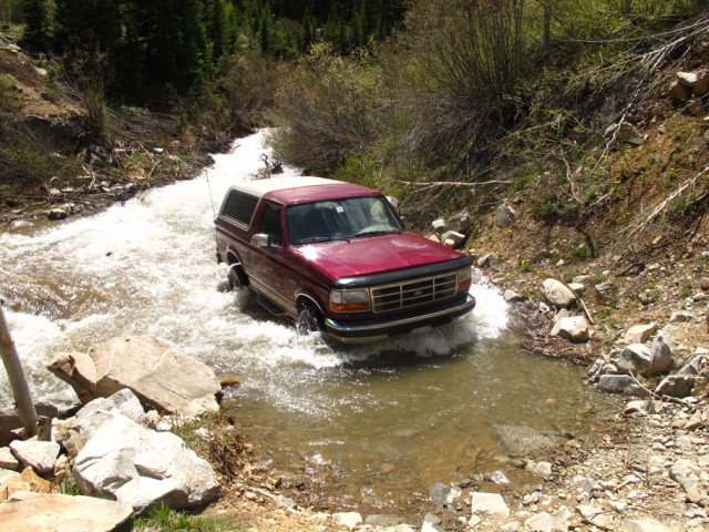 Red 1996 Ford Bronco driving through a rocky stream.