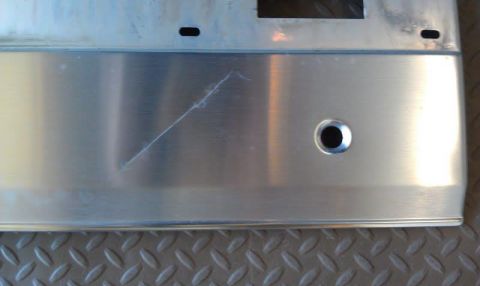 1996 Ford Bronco - A close-up view of a brushed aluminum panel with a scratch and a circular cutout. The panel is mounted on a textured surface.