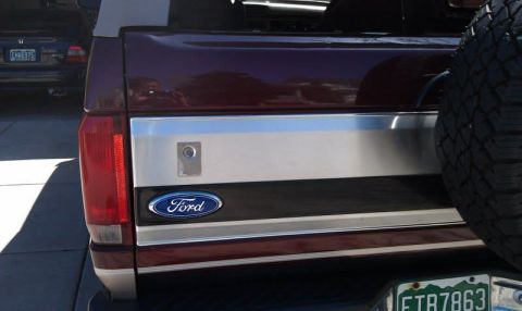 1996 Ford Bronco - Close-up rear view of a maroon Ford Bronco showing the tailgate with a Ford emblem and a spare tire mounted on the right side. A license pl…