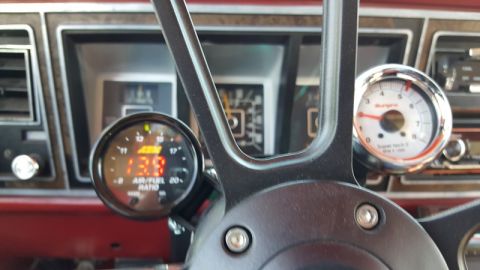 1978 Ford Bronco - A close-up interior shot of a 1978 Ford Bronco shows a black steering wheel with two gauges mounted to it. The left gauge is an AEM Air/Fue…