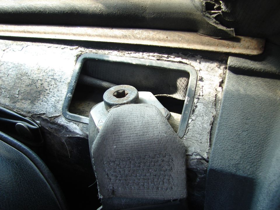 Car interior showing seatbelt buckle and vent opening with worn surfaces.