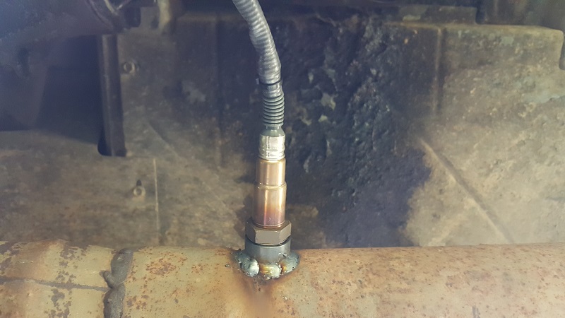 Oxygen sensor installed in a rusty exhaust pipe.